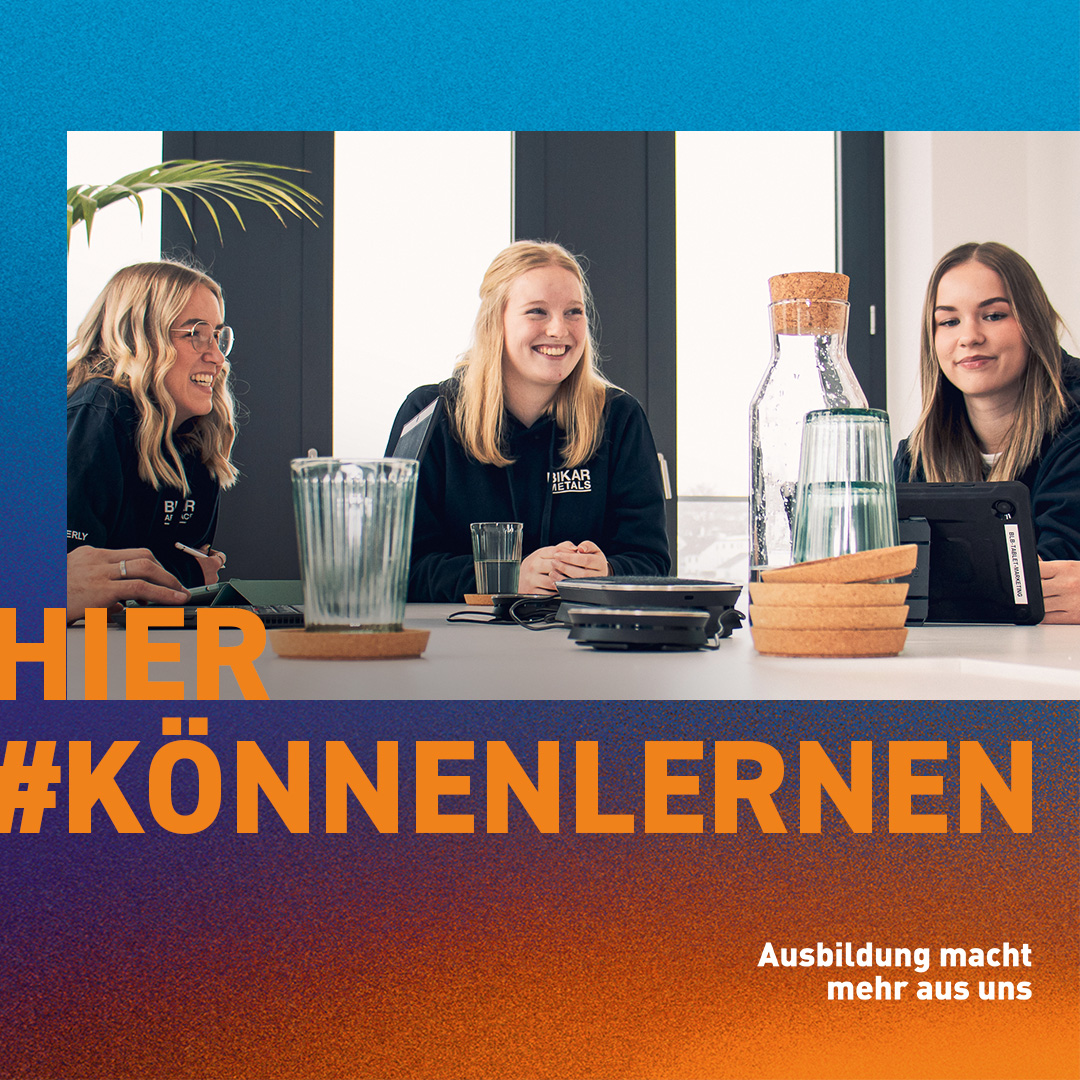Drei junge Frauen von BIKAR METALS sitzen gemeinsam an einem Tisch. Auf dem Banner steht: „HIER #KÖNNENLERNEN“.