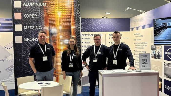 The BIKAR METALS team serving customers in the Benelux region is standing at a trade fair booth and smiling at the camera.