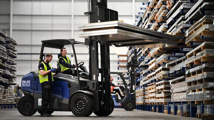 Forklift is in front of a high-bay racking and holding aluminum sheets.