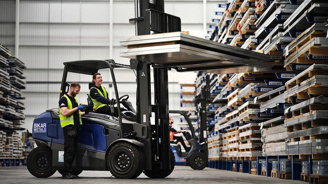 Forklift is in front of a high-bay racking and holding aluminum sheets.
