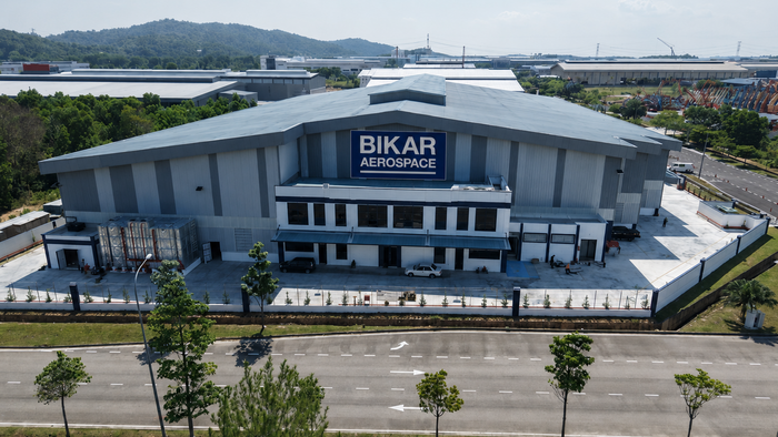 Luftaufnahme des BIKAR AEROSPACE-Werks in Sendayan, Malaysia, mit dem Firmengebäude, der Zufahrtsstraße und bewaldeten Hügeln im Hintergrund.