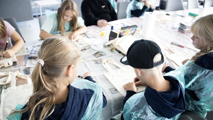 Mehrere Kinder gestalten gemeinsam kreative Kunstwerke an einem mit Zeitungen ausgelegten Tisch.